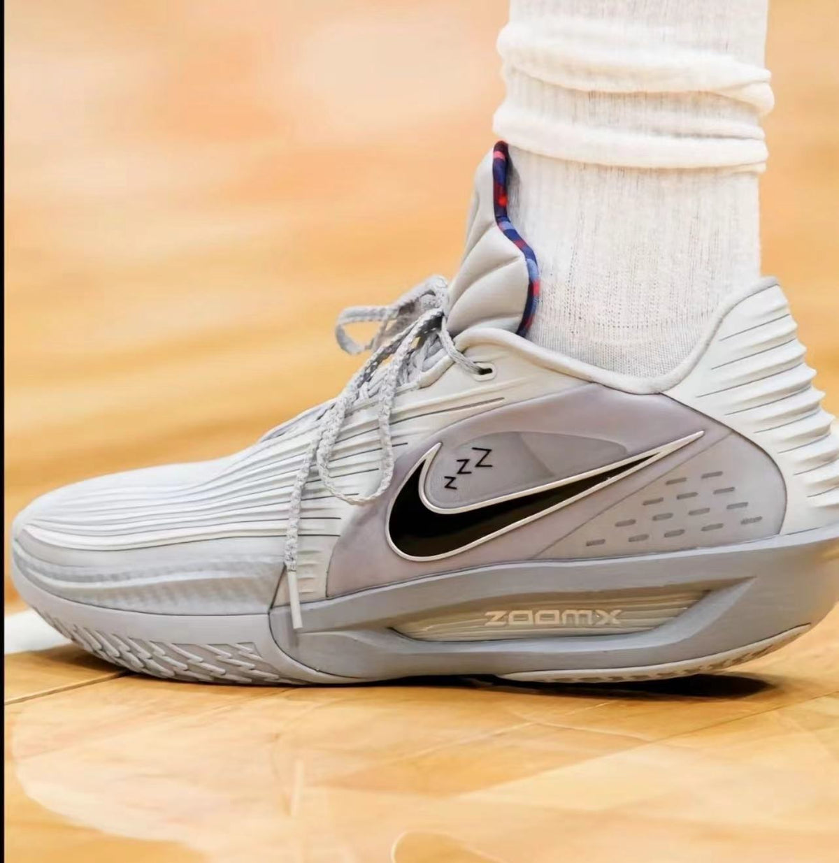 Side view of white and gray Nike sneakers with a black Swoosh and visible ZoomX lettering on the midsole.
