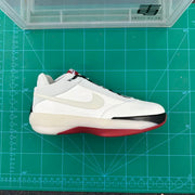 Side view of white Jordan basketball sneakers with black and red accents on a green cutting mat.