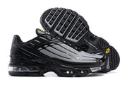 Side view of black and grey Nike Air Max Plus sneakers showing the outsole and visible cushioning.