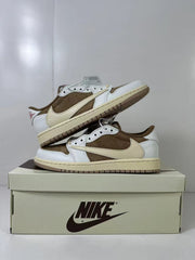 Two low-top sneakers displayed on a shoebox, highlighting the white and brown upper, cream Swoosh, cream midsole, and brown outsole.