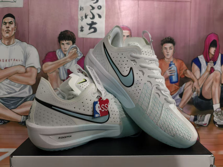 Pair of white Nike basketball sneakers displayed on a box, showing light blue-green Swoosh accents, perforated uppers, and ZoomX midsole branding.