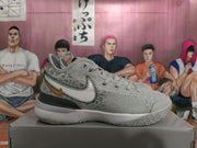 Side view of a silver Nike basketball shoe with a large stitched Swoosh and gold-tone accent
