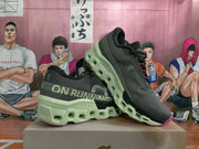 Two dark On Running sneakers displayed at an angle, showing lime-green soles and pink accents.