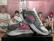 Pair of white, gray, and pink Nike basketball-style sneakers displayed on a black box.
