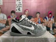 Side profile showing the woven upper, white Nike Swoosh, speckled midsole overlay, black side panel, and gray outsole.
