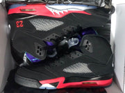 Pair of black high-top sneakers in a box, showing red midsoles, purple accents, and perforated side panels.