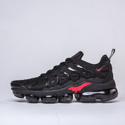 Side profile of a black sneaker with red accents and a segmented outsole.