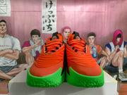 Front view of the pair showing orange uppers, orange laces, black accents, and bright green toe outsoles.