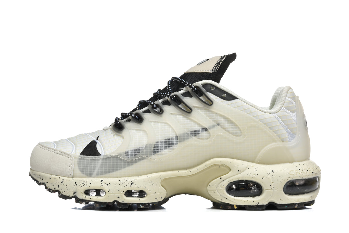 Side view of a cream and black Nike sneaker with translucent layered panels, patterned black laces, and visible air-cushion units.