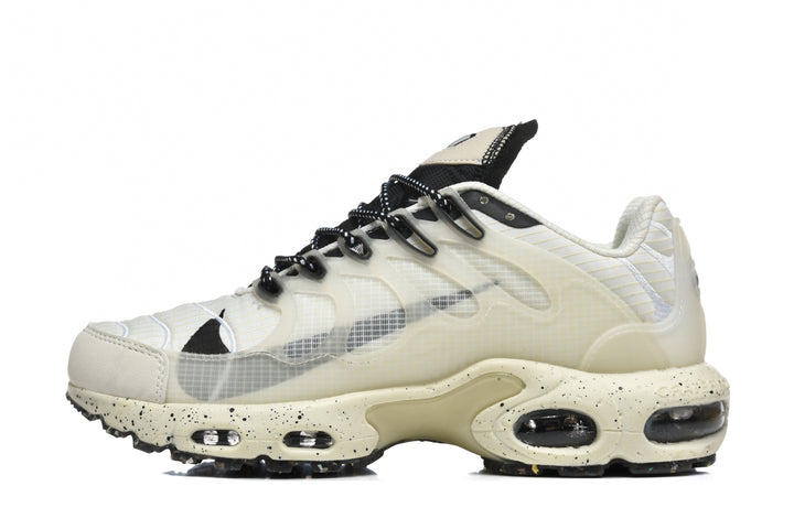 Side view of a cream and black Nike sneaker with translucent layered panels, patterned black laces, and visible air-cushion units.