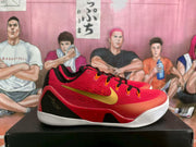 Side view of red Nike basketball sneakers showing gold Swoosh branding, black heel panels, orange lace loops, and white outsoles.