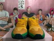 Front view of the pair showing yellow laces, tonal toe panels, tongue emblems, and green midsoles.