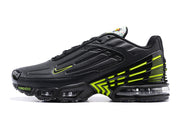 Side profile of a black Nike Air Max Plus sneaker with volt accents and visible air units.