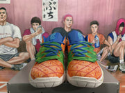 Front view showing orange pineapple-inspired toe boxes, green overlays, blue laces and blue tongue panels.