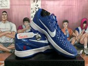 Pair of blue Nike Kobe basketball shoes shown from the side and at an angle, with white swooshes and red details.