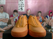 Front view of the tangerine-orange sneakers showing the center zippers and tonal upper panels.