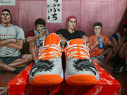 Front view showing white laces, orange uppers, gray patterned toe panels, and orange outsoles