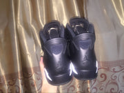 Rear view of the sneakers being held against a patterned curtain, showing heel branding and white accents.