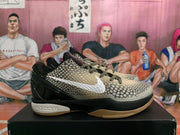 Side view of a Nike basketball sneaker showing the beige textured upper, white Swoosh, glossy black heel, black midsole section, and visible Nike Zoom branding.