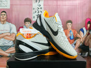 Pair of white, black, and yellow-orange Nike Kobe basketball shoes shown from the side.