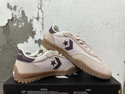 Pair of cream Converse trainer-style sneakers with pale pink panels, plum accents, and gum-colored outsoles
