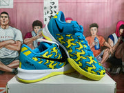 Angled view showing the blue and yellow patterned Nike sneakers, laces, heel details, white midsole, and yellow outsole.