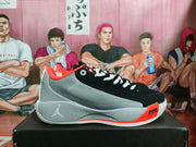 Side view of a black and gray Jordan basketball sneaker with white laces, orange accents, and visible Air Zoom marking.