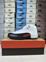 Jordan Air Jordan 12 sneaker displayed side-on on its shoebox, showing the white upper, black forefoot and red accent.