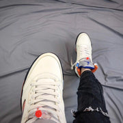 Top view of the white sneaker showing the toe box, white laces, tongue, and blue and orange collar details.