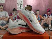 Angled view of the white Nike sneakers showing the black Swoosh, yellow lace details, and pink-orange sole structure.
