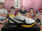 Side view of a white Nike basketball sneaker with a black Swoosh, black heel, and yellow outsole accent.
