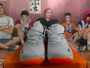 Front view of gray and white Nike basketball shoes with dark accents and bright orange outsoles.
