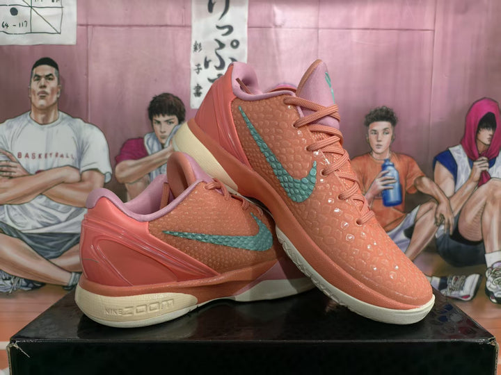 Pair of coral-orange Nike basketball sneakers with green Swoosh branding, pink collars, textured uppers, and cream midsoles displayed on a box.