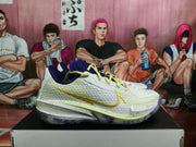 Side view of white Nike basketball sneakers with purple lining, yellow laces, gold Swoosh detailing, and a translucent purple-accented outsole.
