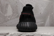 Rear view of a black sneaker showing the ribbed heel sole and red stitching across the heel loop.