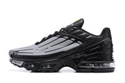 Side profile of a black and grey Nike Air Max Plus sneaker.
