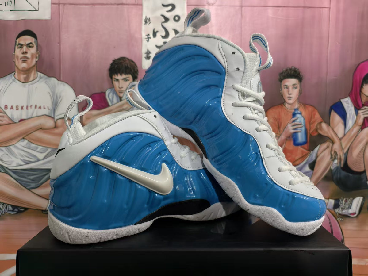 Pair of white and blue Nike Foamposite-style basketball sneakers shown from a three-quarter front and side angle.