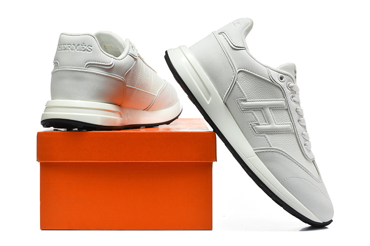 White low-top sneaker pair with tonal side details, shown beside an orange box.