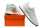 White low-top sneaker pair with tonal side details, shown beside an orange box.