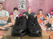 Front view of black Nike sneakers showing the perforated-texture upper, black laces, glossy toe overlays, and padded tongues.