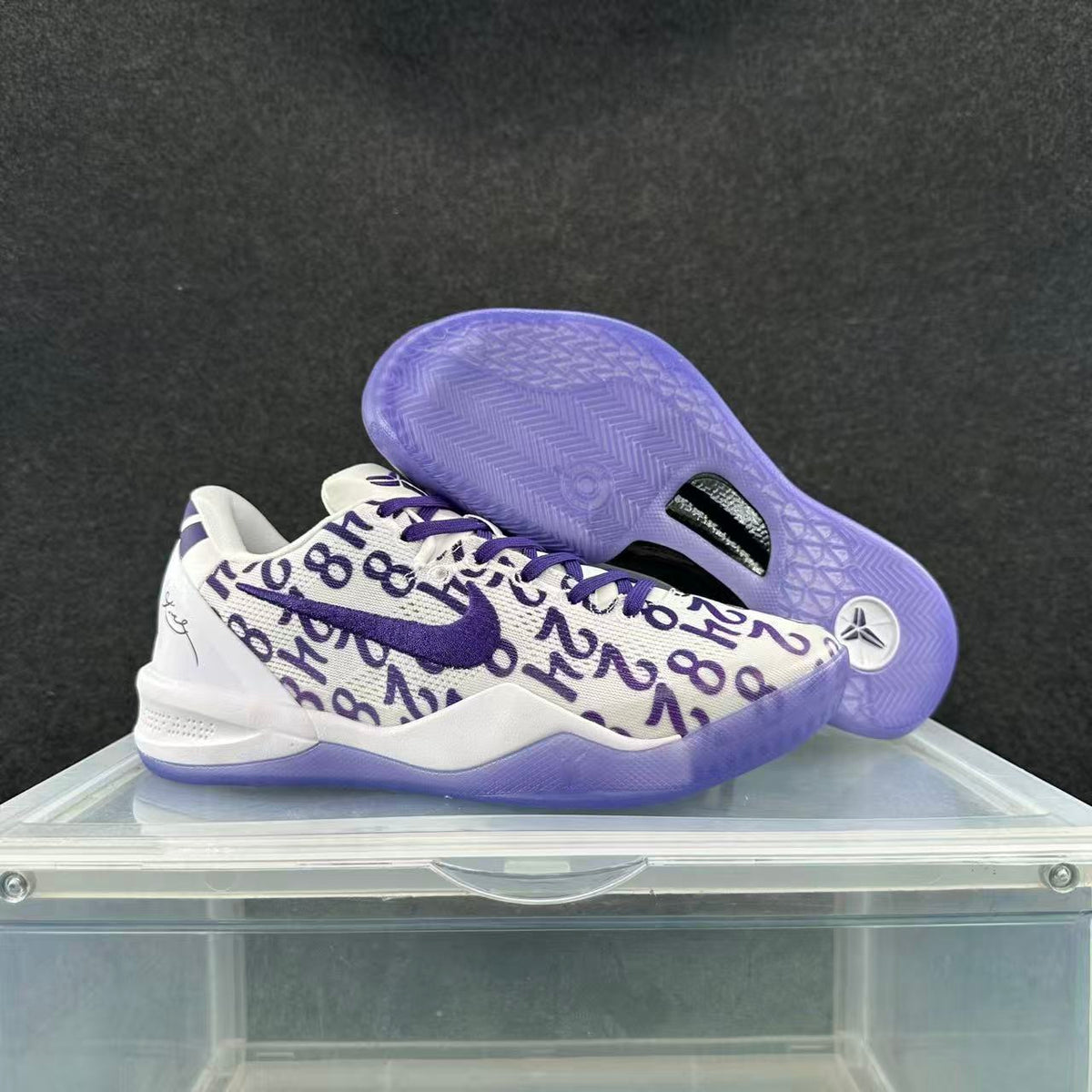 Pair of white and purple Nike basketball sneakers showing the patterned upper, purple Swoosh, laces, and translucent outsole.