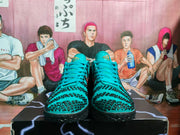 Front view of the teal and black sneakers showing the lacing, patterned toe areas and textured black outsoles.