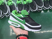 Black and green low-top sneaker with white trim and a visible heel air unit, shown in hand among similar shoes.