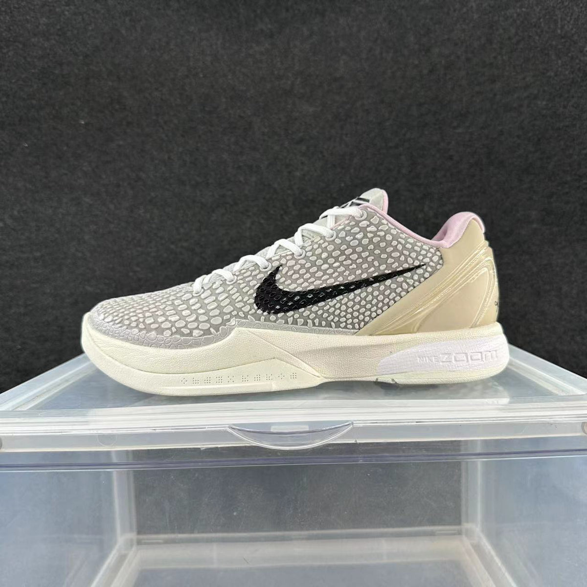 Side view of a gray patterned Nike basketball shoe with a black Swoosh, pale yellow heel panel, pink collar lining, and light sole.
