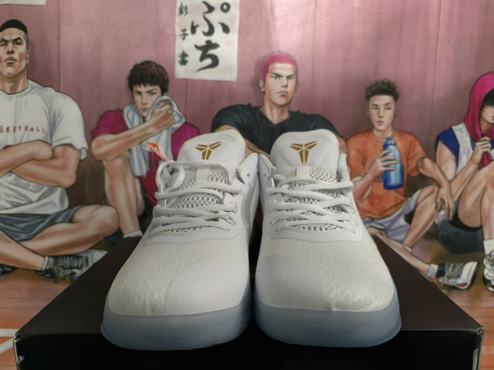 Pair of white Nike basketball sneakers shown from the front, with gold Kobe emblems on the tongues and a translucent outsole.