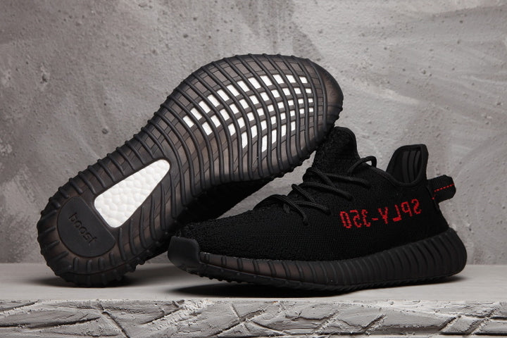 Black Yeezy 350 V2-style sneakers shown from the side and sole, with red side lettering and a ribbed black outsole.