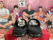 Pair of black Nike slides viewed from the front, showing the cushioned sole and Nike-branded box.