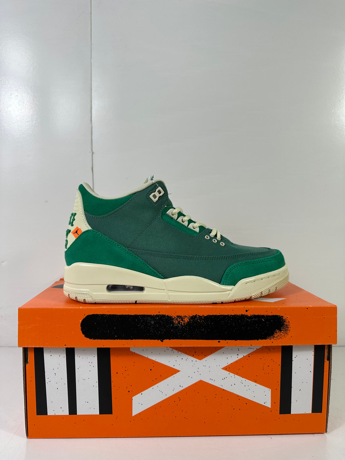 Green and off-white high-top sneaker displayed on an orange Jordan shoebox.