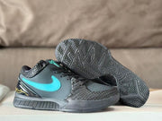 Black and turquoise sneaker pair with one shoe lifted to display the patterned rubber outsole and visible traction design.