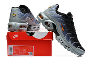 Nike Air Max Plus sneakers in black, grey and orange beside a box showing a sample size label